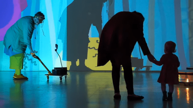 Two people bent down holding the hand of a child