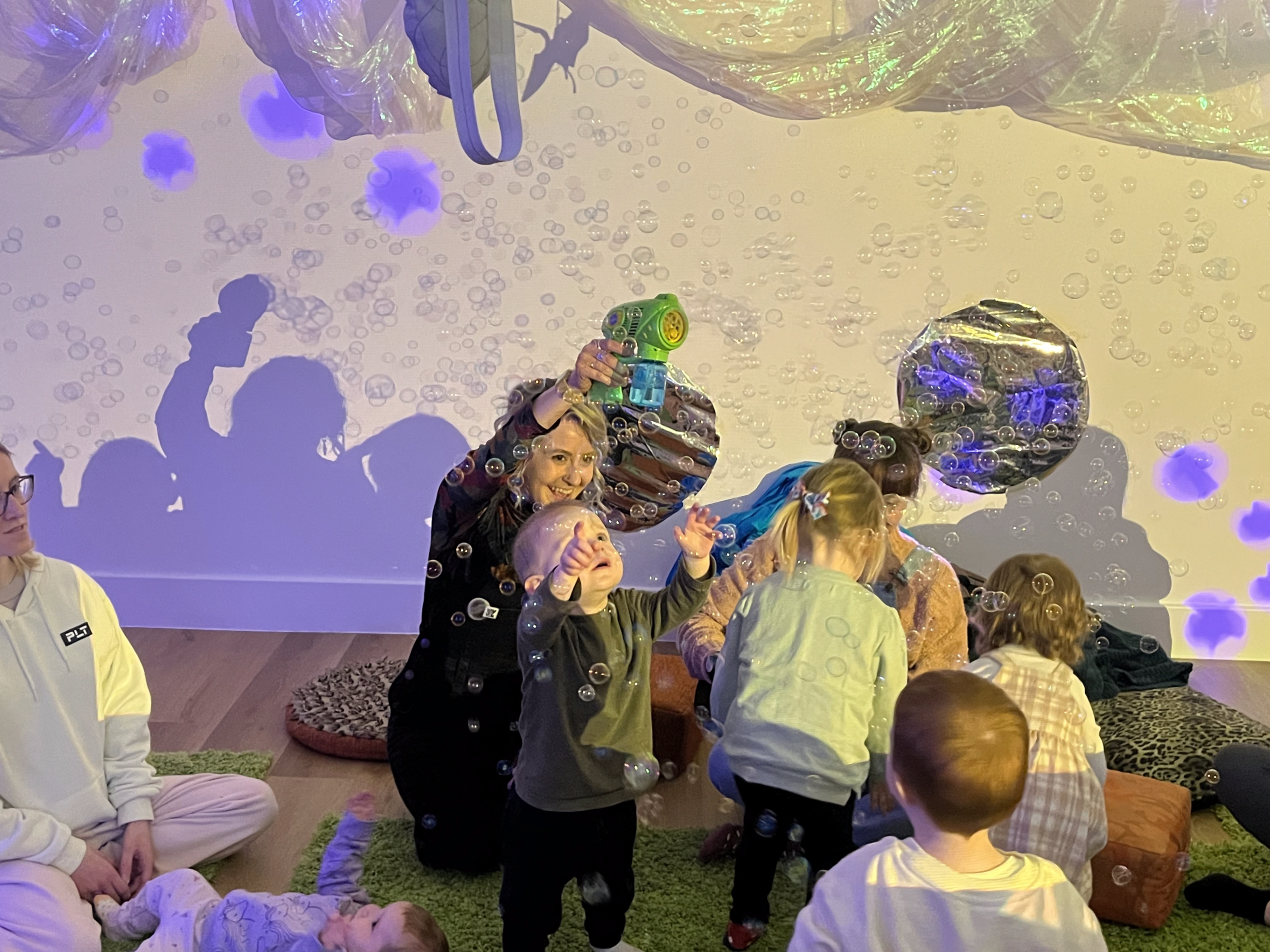 Woman holding bubble machine while toddlers play