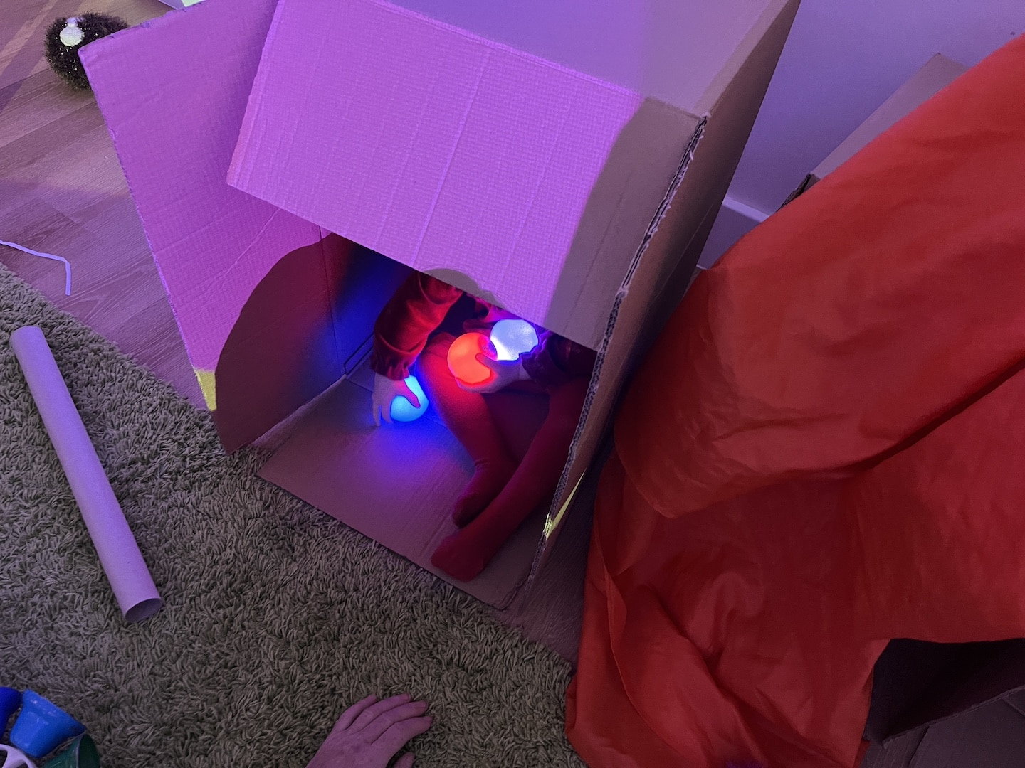 Child playing with light-up balls inside a cardboard box