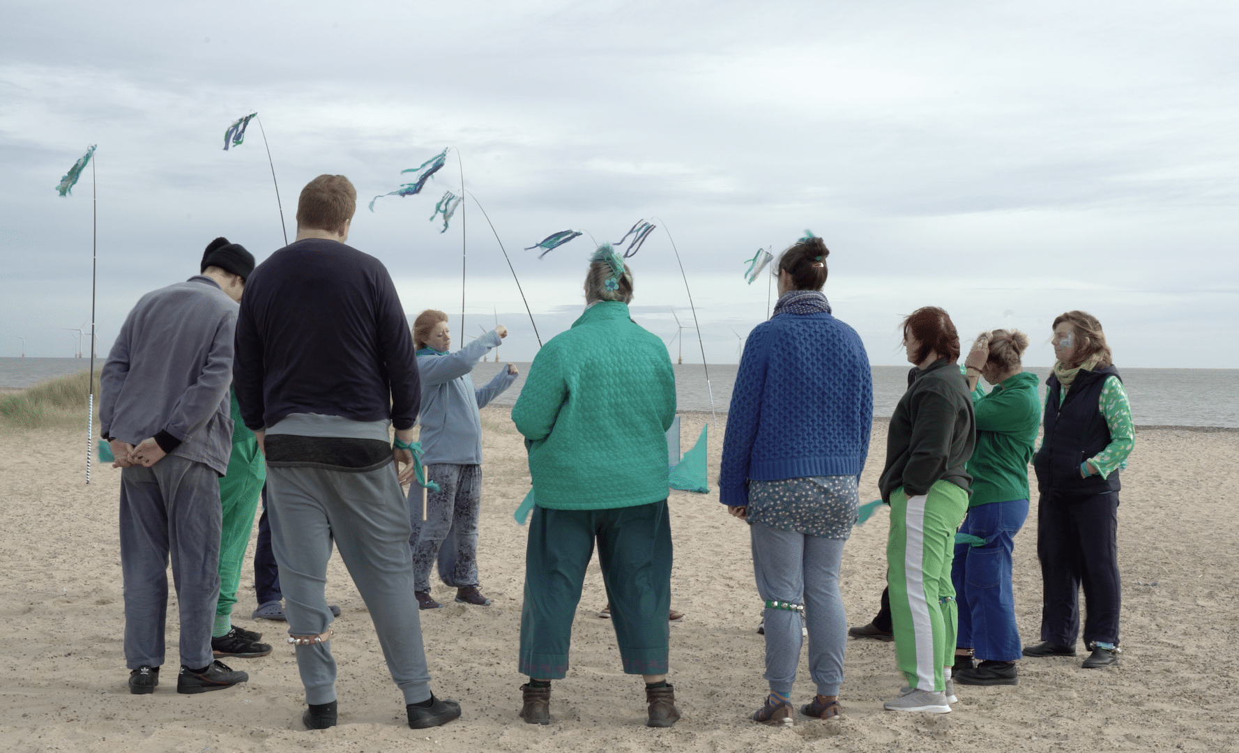 Group of people on a beach holding sticks with tails attached to the top