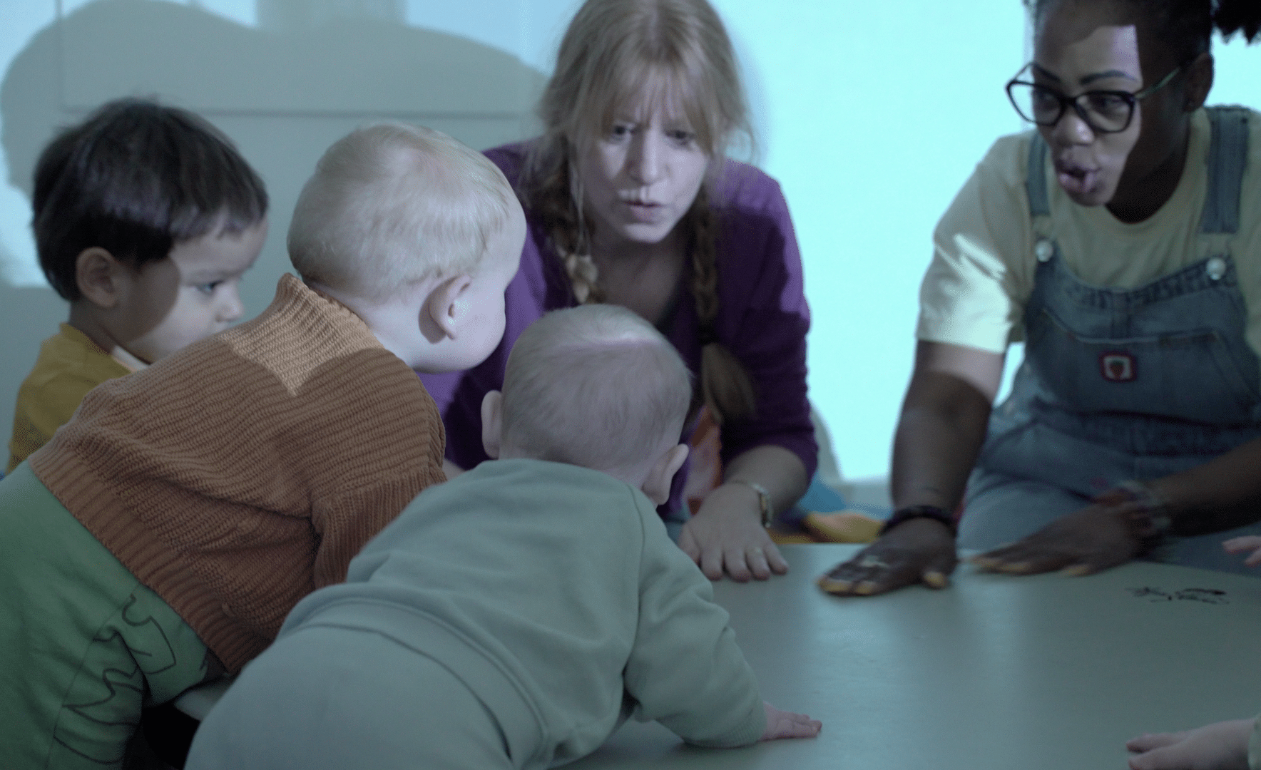 Three babies on the floor and two adults engaging with them